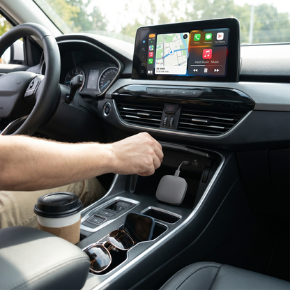 Car interior with a person using a smartphone, cup holder with a coffee cup, and sunglasses plus 3-in-1 Wireless CarPlay Adapter.