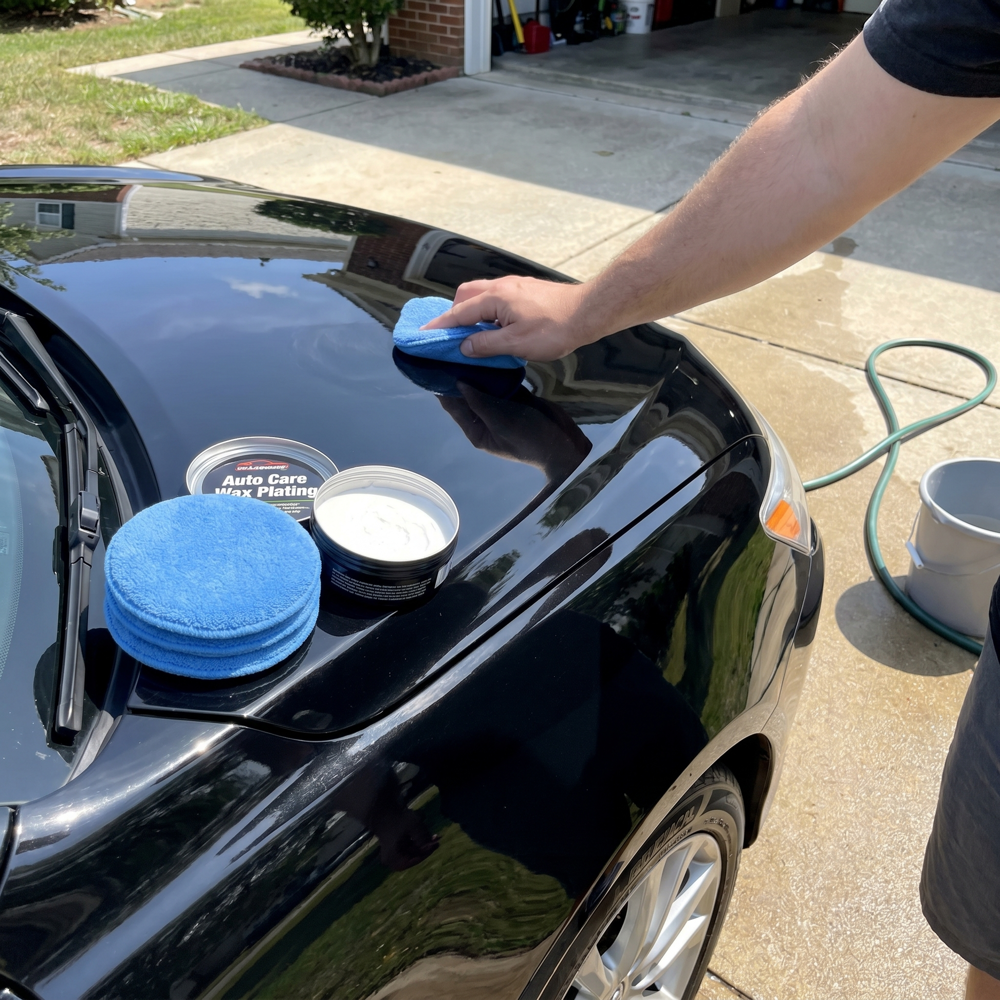 Person applying car wax to a black car with a blue microfiber applicator pad.