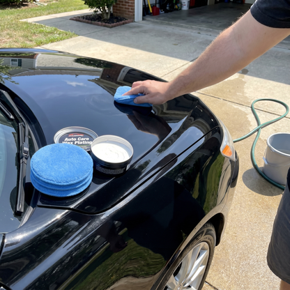 Person applying car wax to a black car with a blue microfiber applicator pad.